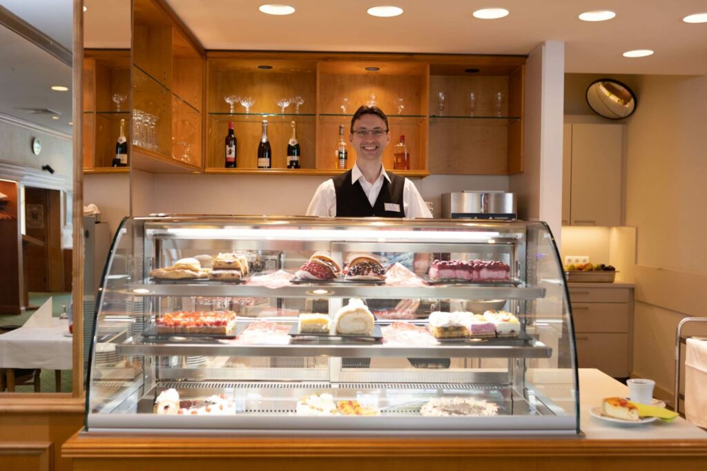 Der Leiter des Servicebereichs Vitali Brodel steht hinter der mit Torten und Teilchen gut bestückten Kuchentheke.