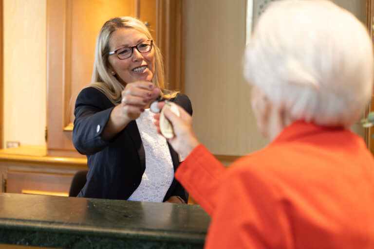 Die Rezeptionsleitung Frau Burmann übergibt einer Bewohnerin einen Zimmerschlüssel.