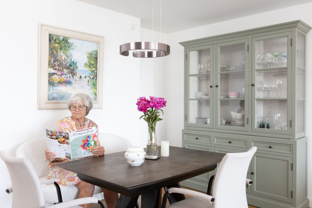 Eine Bewohnerin sitzt am Esstisch in ihrem Appartement und liest die Frühlingsausgabe des ResidenzBoten.