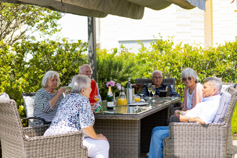 Auf der Dachterrasse: Eine Gruppe von Senioren sitzt vor der Sonne geschützt im Schatten beim Kartenspiel.