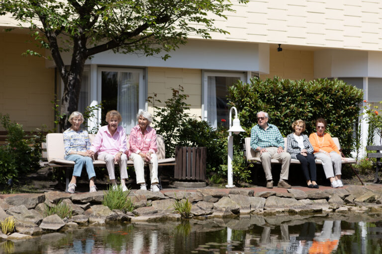 Einige Bewohnerinnen und Bewohner genießen die Frühlingssonne am Teich vor der Residenz.